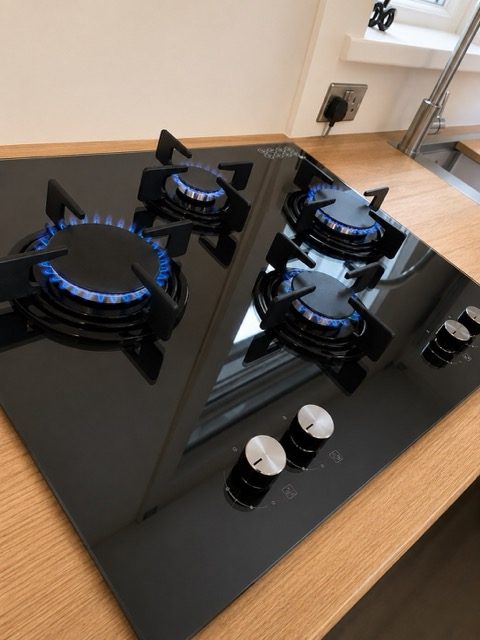 Black glass gas hob installed by Plumbforce, burners lit